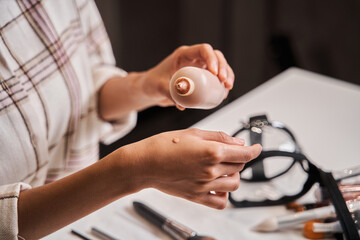 Blogger woman putting drop of her tone cream at hand while broadcasting make up tutorial
