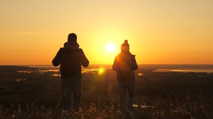 Free travelers, man and woman with backpacks, descend from mountain in rays of dawn, enjoy nature, beautiful sun and landscape. Carefree tourists travel at sunset. Teamwork in business.