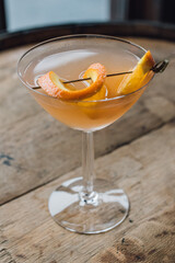 citrus orange grapefruit cocktail in coupe stem glass sitting by window on wood barrel