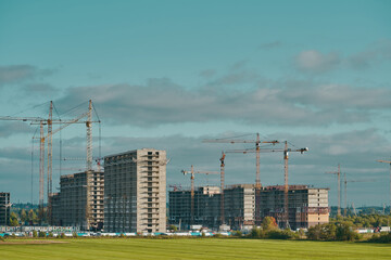 Industrial building cranes, multi-storey buildings of new city districts and large green field. Project of urban area. Construction site background with copy space.