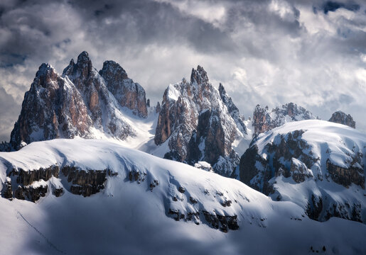 Beautiful mountain peaks in snow in winter. Dramatic landscape with high snowy rocks, overcast sky with clouds in cold evening. Tre Cime in Dolomites, Italy. Alpine mountains. Nature. Dark scenery