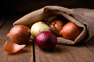 Red and white onions on a rustic wooden table spilling out of a cloth sack in the kitchen, top view. High quality photo