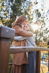 Naklejka premium Lovely woman and her teen daughter embracing at the urban park outdoors