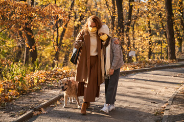 Mother and daughter wearing protective masks bonding to each other while walking
