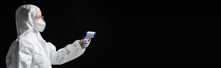 side view of doctor in personal protective equipment holding pyrometer isolated on black, omicron...