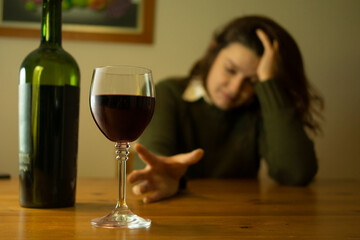 Close-up of a woman with a green jacket sitting alone at a table trying to reach a glass of red wine with her hand