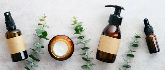 Natural organic cosmetics in amber glass bottles in row on stone table with eucalyptus. Beauty blog...
