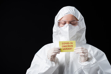 scientist in white hazmat suit and goggles holding card with covid-19 omicron variant lettering...