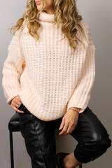 Woman wearing black leather jeans and with a powder pink turtleneck sweater. Trendy casual outfit. Details of everyday look. Street fashion.