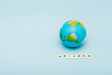 white cubes with omicron lettering near globe on blue background with copy space.
