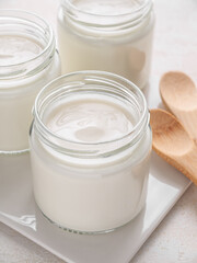 Fototapeta na wymiar Glass jars of homemade plain yogurt with wooden spoons on white tray. Vertical. Close up.