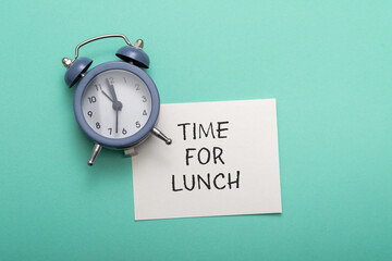 Conceptual photo of an alarm clock with a note and text Time for lunch on a blue background.