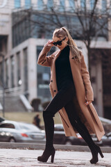 Young beautiful girl in a beige coat and sunglasses walks through the city