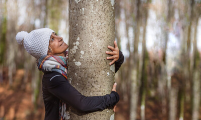 a woman in a white cap hugs a tree in a forest while looking at it with affection.concept love for...