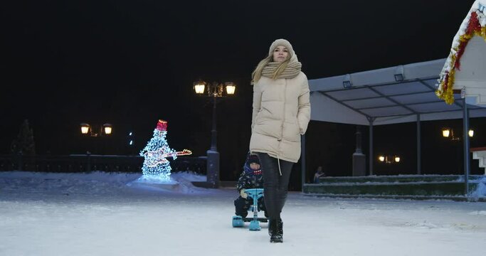 Young Cute Mom Is Driving Her Little Son On A Sled, Front View