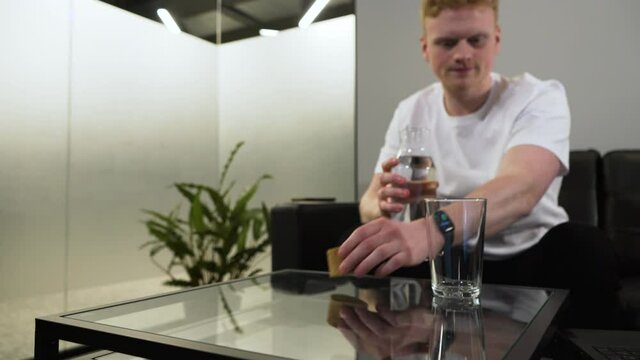 Caucasian man pouring a cup of water into a glass - sitting on a sofa