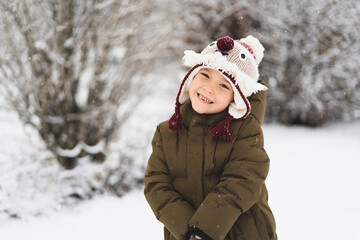 Child enjoying winter. Cute little boy in funny winter hat walks during a snowfall. Outdoors winter activities for kids. Winter Christmas and lifestyle concept.