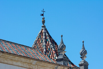 Old colored roof tiles with a vane, a cross and ornaments in Coimbra, Portugal.