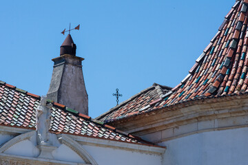 Old colored roof tiles with a vane, a cross and ornaments in Coimbra, Portugal.