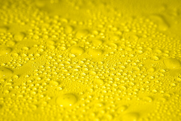 Transparent water droplets from spray on yellow background. Selective focus