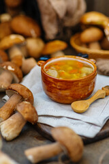 A plate of mushroom soup in the shape of a deer standing on a wooden table surrounded by porcini mushrooms