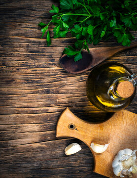 Food background, top view of rustic kitchen table with wooden cutting board, cooking spoon, olive oil, parsley and garlic.