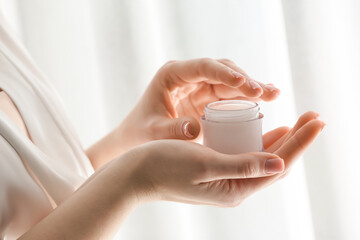 Young woman with jar of cosmetic cream at home