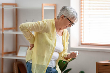 Senior woman with pills suffering from back pain at home