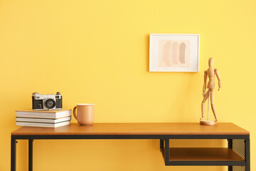Workplace with books, cup and wooden mannequin doll near color wall