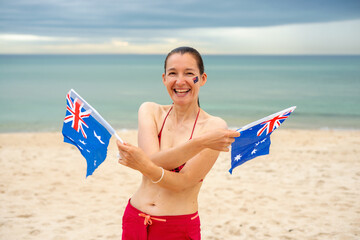 Happy woman waving two small Australian flags at the beach. 
