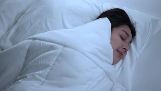 Beautiful asian woman lying in the bed at night. Young woman sleeping well in comfortable cozy fresh bed on soft pillow white linen. Health and rest concept.