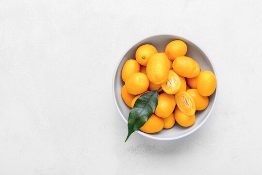 Bowl with tasty kumquat fruits on light background © Pixel-Shot