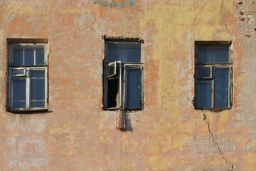 Three rotten windows in the yellow plastered wall of a ruined old brick house