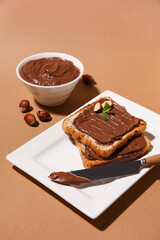 Plate of bread with chocolate paste and hazelnuts on beige background