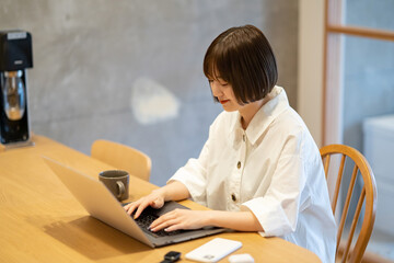 自宅の部屋でノートPCを操作する若い女性
