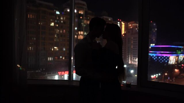 of a couple in love kissing against the background of a panoramic window overlooking the night glowing city. Secret meeting of lovers at the hotel. The concept of love in the city. Valentine's Day.