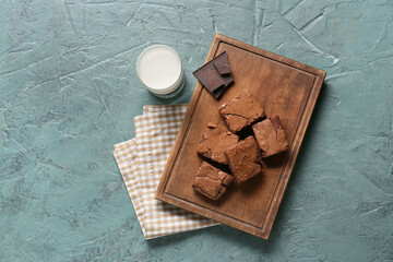 Wooden board with tasty chocolate brownie pieces and glass of milk on green background
