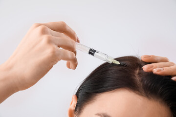 Young woman with hair loss problem giving herself injection on light background