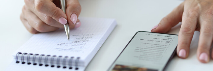 Woman is rewriting prescription from smartphone into notebook