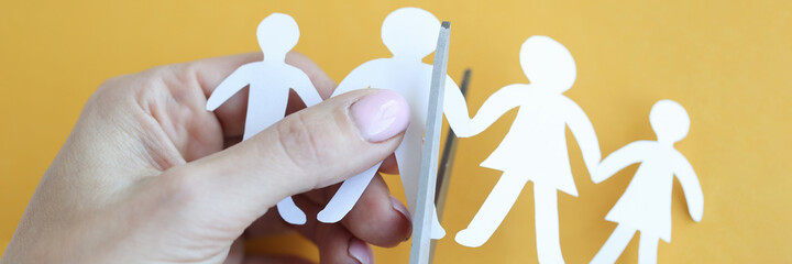 Woman hand cuts paper figures in form of family with scissors closeup