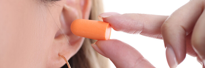 Woman inserts soft orange earplugs into ear closeup