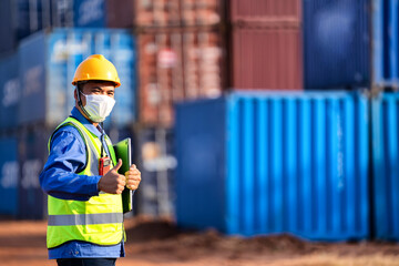 An industrial worker wearing a yellow protective cap holds a laptop to inspect the container yard.