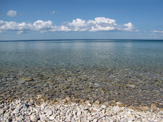 a beautiful scenic view of stones through the shallow water under a blue sky