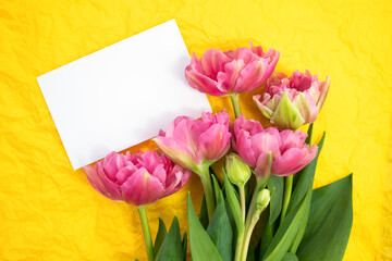 Bouquet of fresh tulips and a blank sheet of paper on a yellow background. flat lay, place for text.