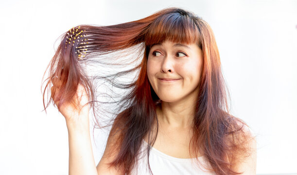 Woman brown-haired with messy on a white isolate background. Shocked female in panic because of hair loss. Hair with a comb in hand having serious hair fall damaged caused by pollution and coloring.