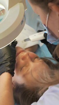 Cosmetologist cleans skin using ultrasonic cleaning device. Doctor's hands in gloves are running metal plate over the client's face. Rejuvenation procedure,treatment of acne and pimples