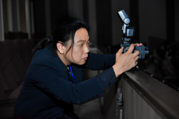Asian long hair photographer in navy suit concentrated with his camera.
