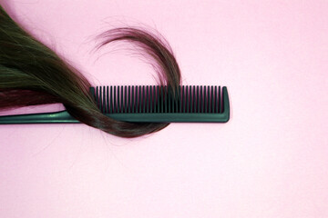 A lock of female light brown hair, a comb on a pink background.