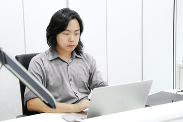 Asian long hair guy focuses and concentrates on his work in front of laptop in the office.