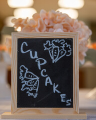 a chalkboard sign with the word cupcakes written on it sits on a table in a cafe
